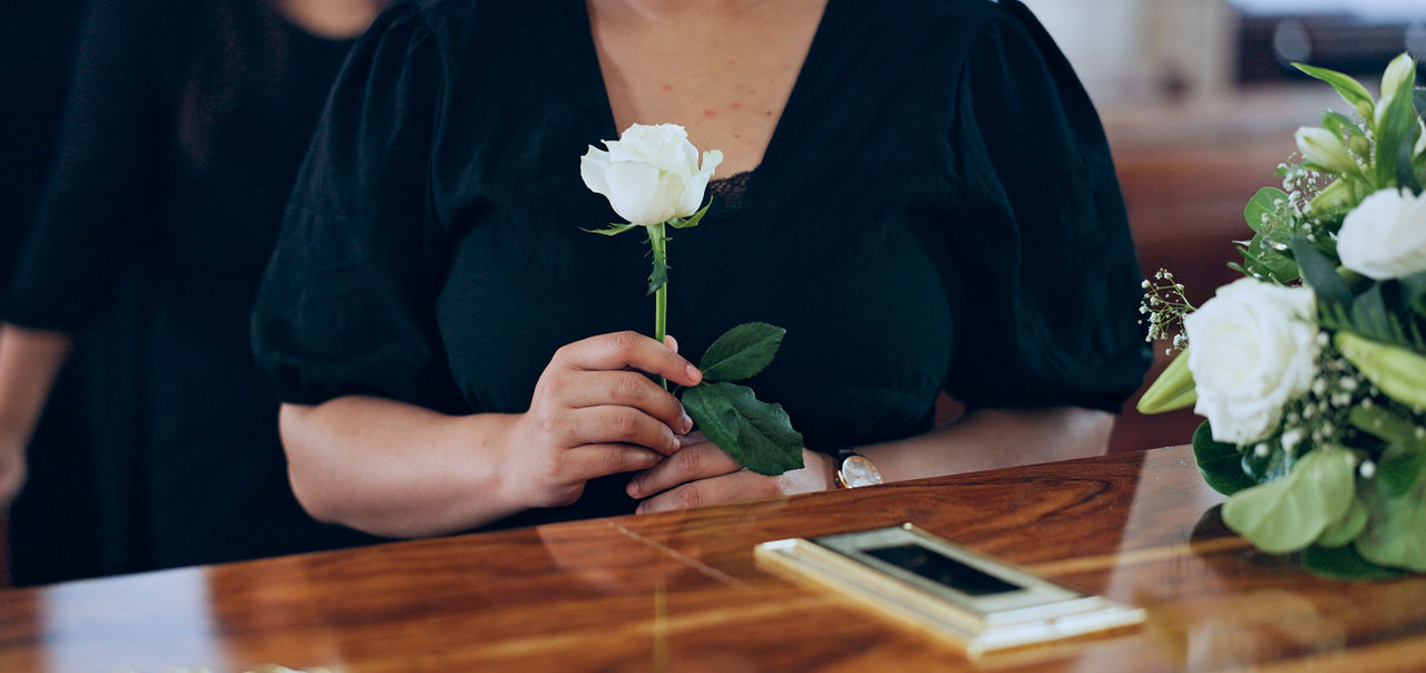 a person laying a white rose on a coffin